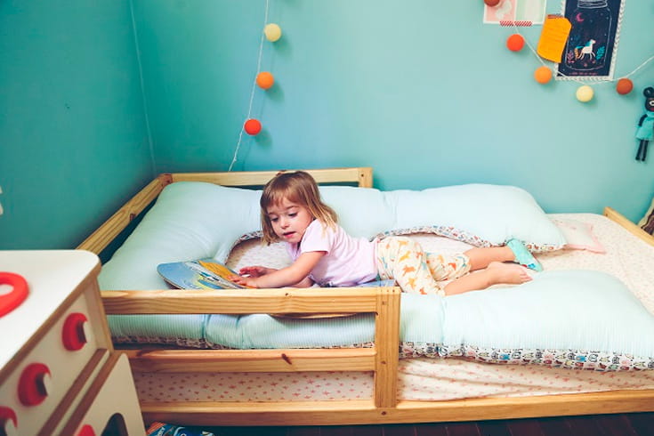 crianca deitada na cama infantil de madeira com um livro na mao