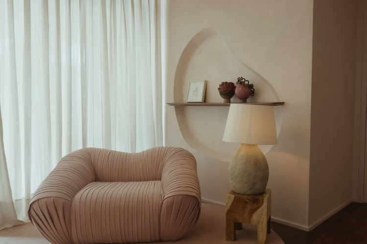 Canto de um quarto com poltrona rosada com textura de várias fendas de costura e prateleira com buraco na parede.