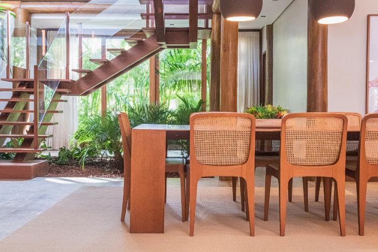 Sala de jantar com conjunto de mesa retangular e 8 cadeiras de madeira robusta e de cor terrosa