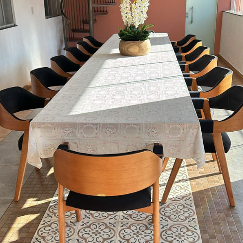 Sala de jantar iluminada com cadeiras ottawa em preto e madeira amêndoa, com toalha de mesa de renda branca.